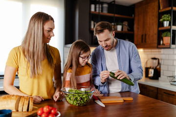 Handsome man, attractive young woman and their cute little daughter are making salad together.