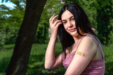 Naklejka premium Smiling female with band-aid on arm after vaccination.. Woman feeling positive after getting vaccinae. Happy teenage girl outdoor