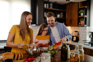 Handsome man, attractive young woman and their cute little daughter are making salad together. Healthy lifestyle.