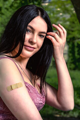 Smiling female with band-aid on arm after vaccination.. Woman feeling positive after getting vaccinae. Happy teenage girl outdoor