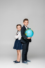 Fototapeta premium happy schoolboy holding globe while standing with girl in dress on grey.