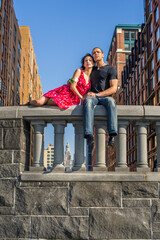 A lovely young couple passionately rely on each other and sit on the top of a wall, guy also holding a white rose..