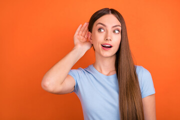 Photo of impressed brown hairdo young lady hand ear look empty space wear blue t-shirt isolated on vivid orange color background