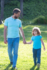 Fototapeta na wymiar happy son and father holding hands walking on sunny summer day in park grass, togetherness