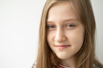 Fototapeta premium portrait of beautiful teenage girl with long hair smiling standing against white wall
