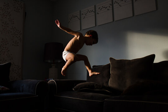 boy in underwear jumps across couches at home
