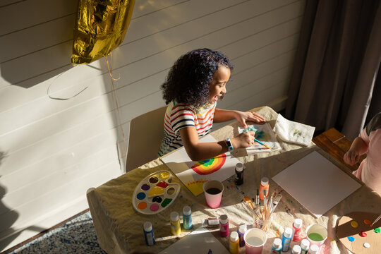 Laughing curly haired girl paints at a table