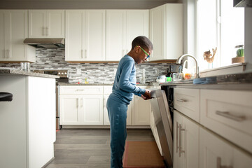 Laughing boy closes dishwasher in bright kitchen