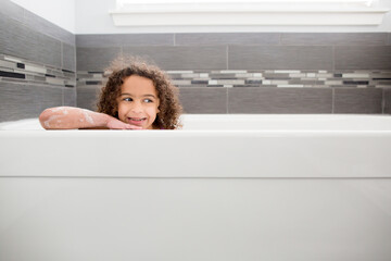 Smiling curly haired girl relaxes in bathtub
