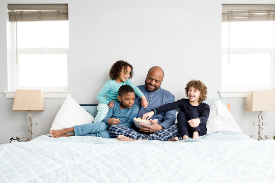 Father and three children eat popcorn on bed