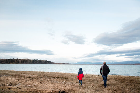 Father and son walk across grass by shoreline
