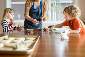 Children decorate sugar cookies at kitchen table with mom