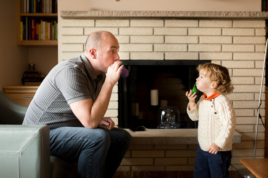 Father and preschooler son blow up balloons in living room