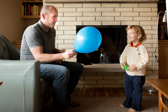 Father inflates balloon for preschooler son