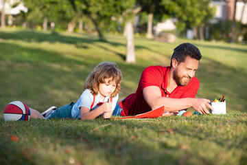 father and son relax on grass in park learning to draw, tutorship