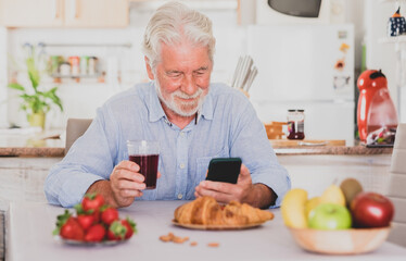 Beautiful senior man white hair having breakfast at home looking social media on smart phone.