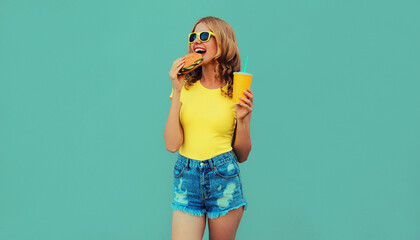 Portrait close up of young woman with fast food, burger and cup of juice wearing a yellow t-shirt,...