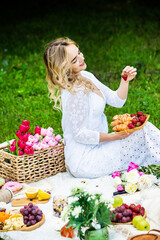 Beautiful woman resting in park sitting on a picnic blanket with fruits and wine. 