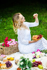 Beautiful woman resting in park sitting on a picnic blanket with fruits and wine. 