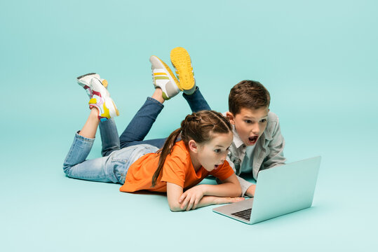 shocked children watching movie on laptop while lying on blue.