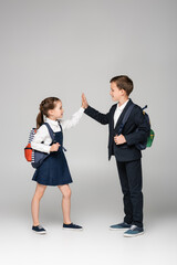 schoolkids with backpacks giving high five on grey.