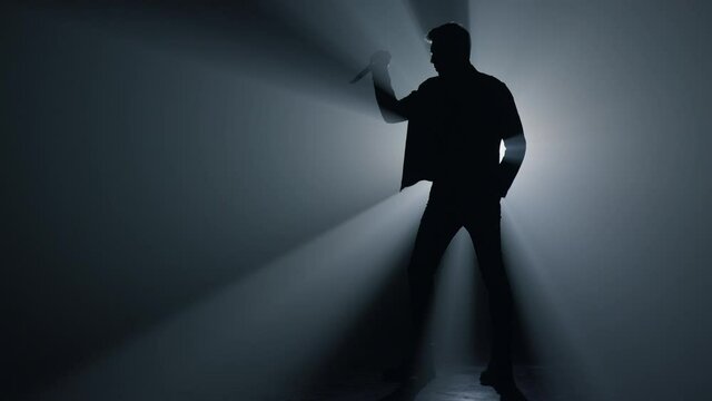 Silhouette offender raising hand with knife in dark. Dangerous criminal weapon.