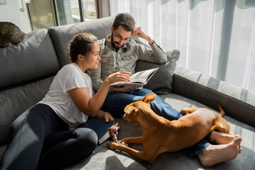 Young couple relaxing and reading in living room with pets