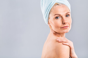 Portrait of smiling senior woman feeling soft skin with hand after spa bath. Mature woman draped in...