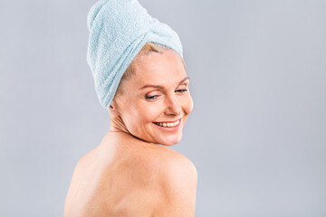 Portrait of smiling senior woman feeling soft skin with hand after spa bath. Mature woman draped in towel looking at camera. Lady in bathrobe after shower isolated over white background.