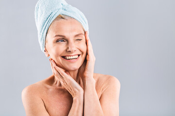Portrait of smiling senior woman feeling soft skin with hand after spa bath. Mature woman draped in...