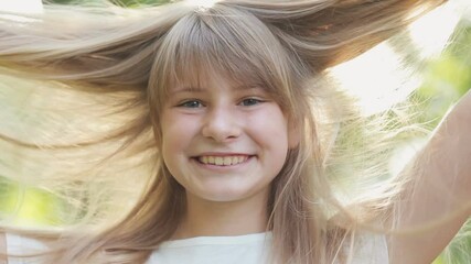 Cheerful young girl with long blonde hair flying outdoor. Portrait of happy smiling girl having fun with her hair.