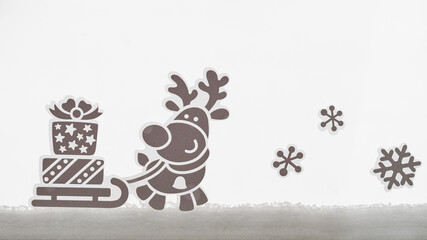 Sticker reindeer pulling a sleigh with gifts on a window with snow.