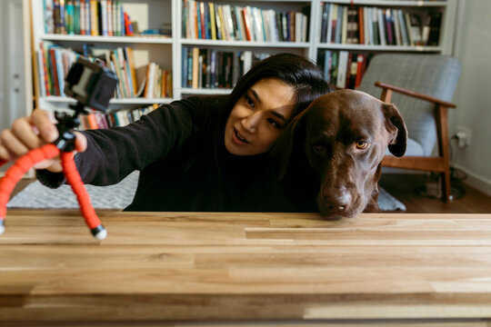 female east asian woman and her labrador dog at home recording a video