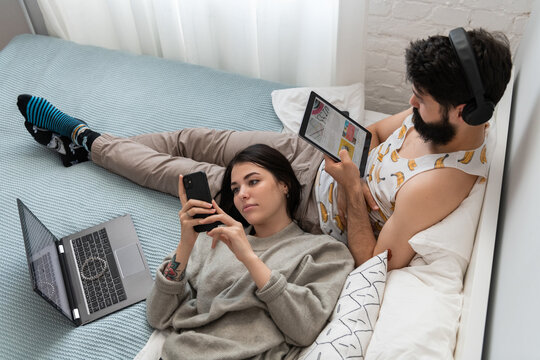Young couple using gadgets and chilling on bed together