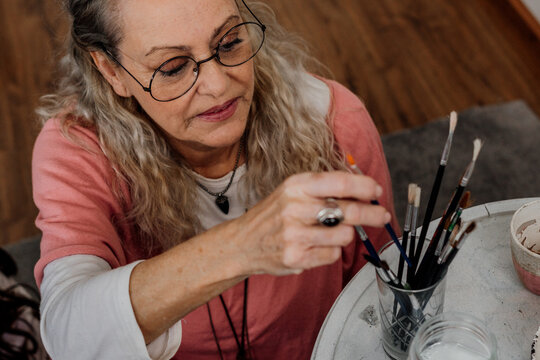 senior woman picking up paint brushes