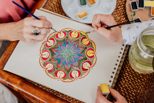 Close-up of grandmother painting mandala with her granddaughter at room