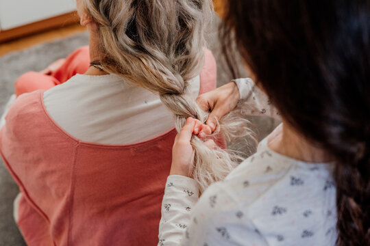 Close-up pf granddaughter making a braid to her grandmother at bedroom 
