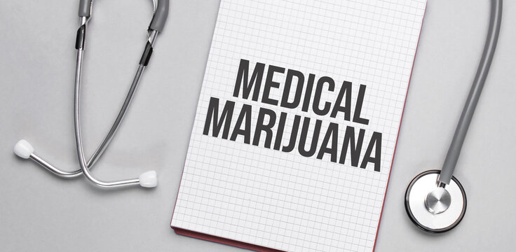 On a beige background, a stethoscope and a white notepad with the inscription medical marijuana. Medical concept