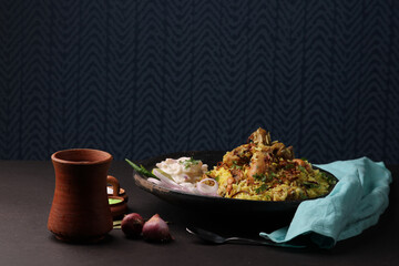chicken dum biriyani served in copper handi or bowl with onion raita.