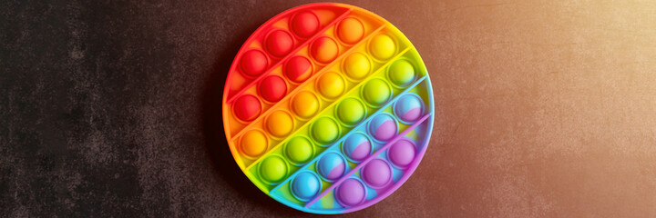 kids anti stress sensory pop it or simple dimple fidget push toy on a black table or floor background. round popit rainbow hue bright color, trend 2021 year. top view, flat lay. banner. flare