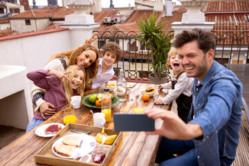 Cheerful family taking selfie during breakfast on terrace