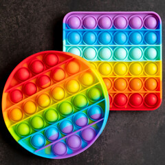 kids anti stress sensory pop it or simple dimple fidget push toys on a black table or floor background. popit rainbow hue bright color, trend 2021 year. top view, flat lay. square