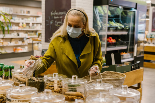 senior woman with protective mask looking spices at waste store