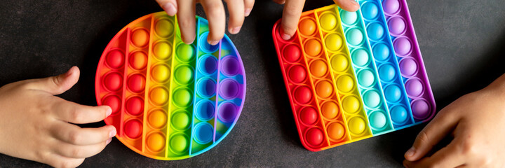 anti stress sensory pop it toys in a children's hands. a little happy kids plays with a simple dimple toy on a black table. toddlers holding and playing popit rainbow color, trend 2021 year. banner