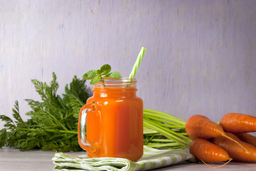 Delicious and healthy juice of young carrots. Orange drink. Carrot juice. Fresh carrots with green leaves. Healthy food.