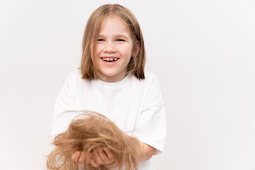 A happy kid girl holds in hands cropped hair after cutting on a white
