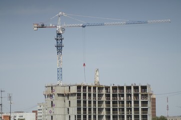 Photo of a city landscape with a construction site. Construction of a high-rise building. Tower crane. Blue sky. In gray, blue and white colors.