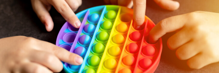 anti stress sensory pop it toys in a children's hands. a little happy kids plays with a simple dimple toy on a black table. toddlers holding and playing trendy popit rainbow color. banner. flare