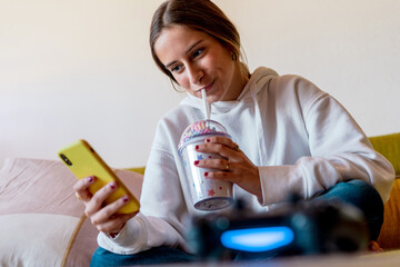 Teenager girl having a smoothie while watching a video on your mobile