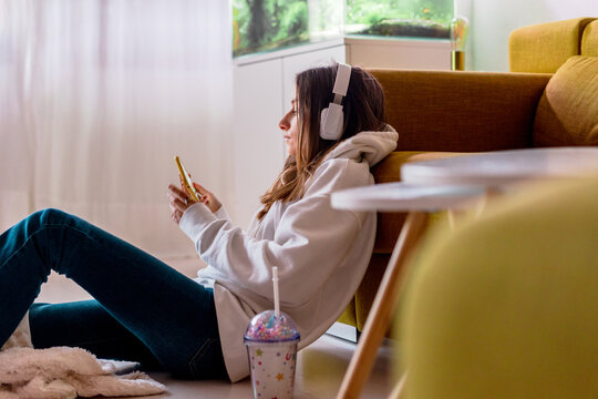 teenager girl listening music with headphones sitting on the floor at home